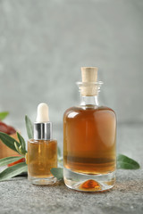 Glass bottles with jojoba oil on stone table against grey background
