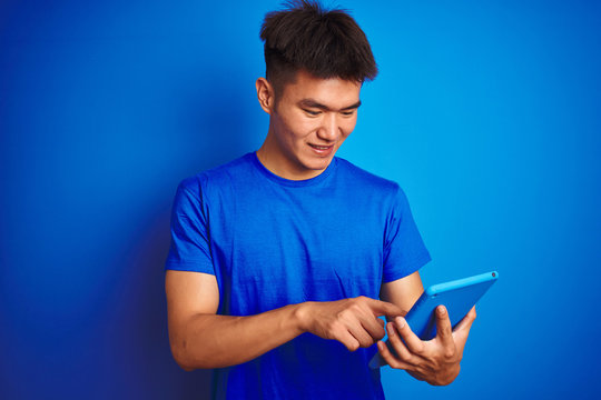 Young Asian Chinese Man Using Tablet Standing Over Isolated Blue Background With A Happy Face Standing And Smiling With A Confident Smile Showing Teeth