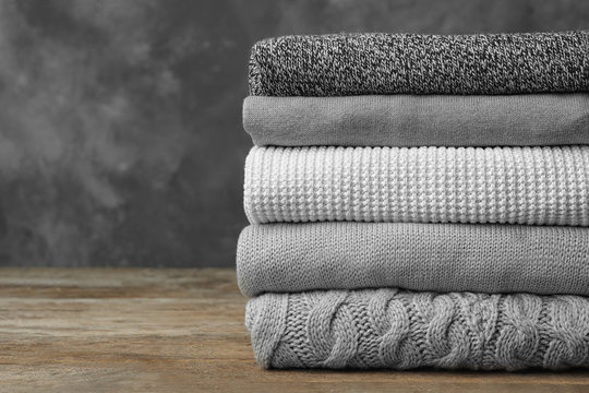 Stack of warm clothes on wooden table against grey background. Autumn season