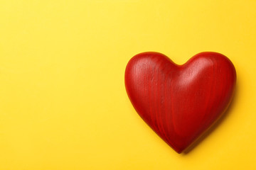 Red wooden heart on yellow background, top view. Space for text