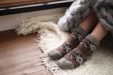 Woman wearing knitted socks on window sill indoors, closeup. Warm clothes