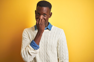 African american man wearing denim shirt and white sweater over isolated yellow background looking stressed and nervous with hands on mouth biting nails. Anxiety problem.