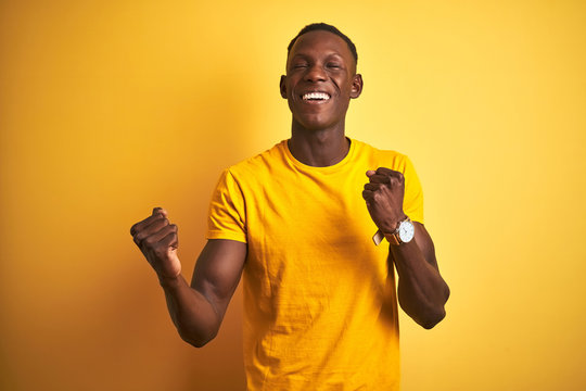 Young african american man wearing casual t-shirt standing over isolated yellow background celebrating surprised and amazed for success with arms raised and eyes closed. Winner concept.