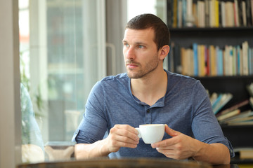 Pensive man holding coffee looking through a window in a bar
