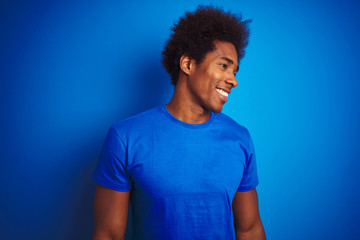 African american man with afro hair wearing t-shirt standing over isolated blue background looking...
