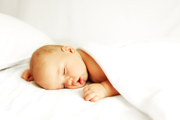 Beautiful baby sleeps on the bed in white sheets.
