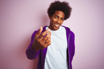 Young african american man wearing purple sweatshirt standing over isolated pink background...