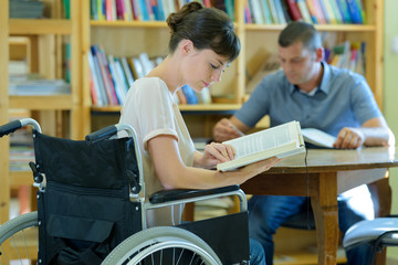 disabled woman in wheelchair reading book in library