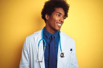 African american doctor man wearing stethoscope standing over isolated yellow background looking...