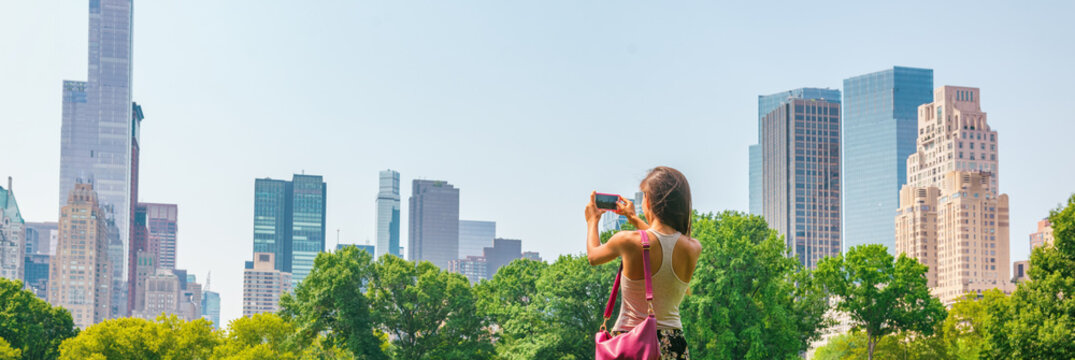 New York City tourist taking photo with phone of NYC Skyline of skyscrapers buildings towers in summer travel vacation panoramic banner background.