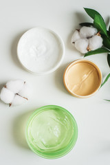 Obraz na płótnie Canvas Jars of cream, aloe gel and moisturizing face patches on a white background next to cotton flowers. Nature Cosmetics for skin care, a means to moisturizing. Natural cosmetics from flower extract