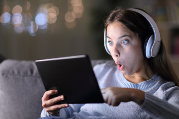 Surprised woman with headphones checks tablet content