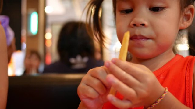Happy little Asian child girl with her sister eating french fries in restaurant. Health care and food concept.
