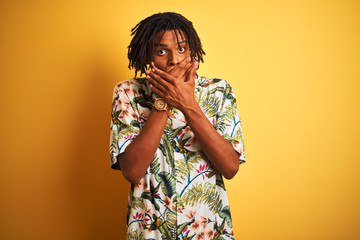 Afro man with dreadlocks on vacation wearing summer shirt over isolated yellow background shocked covering mouth with hands for mistake. Secret concept.