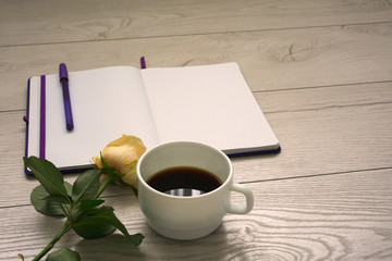 note book empty blank open page with blue pen, tea yellow rose and cup of coffee on wooden desktop in office