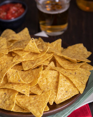 Famous Mexican snack, nachos with guacamole, red chilli sauce and beer on wooden table. Mexican cuisine background