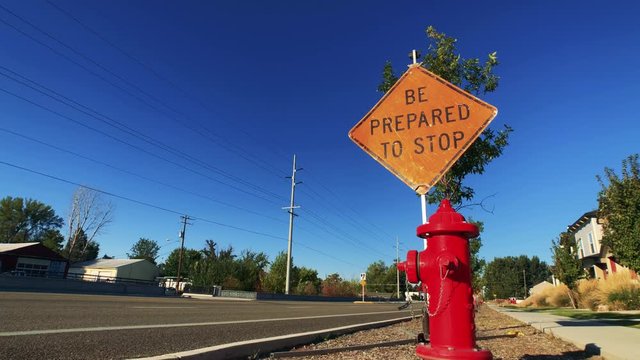 A construction sign that reads, " Be Prepared to Stop" is placed next to a street as traffic zooms by the sign. 
The clip is a time lapse.