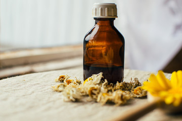 Herbal tincture in pharmacy bottle, dry chamomile flowers and blurred yellow flower of calendula in...