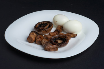 Mushrooms and boiled eggs on a white plate isolated on a black background.Natural food
