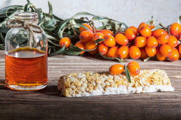 Energy bar with sea buckthorn berries on a wooden background. Sea buckthorn berries on a branch and sea buckthorn oil in a glass vial.
