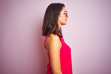 Beautiful woman wearing funny pink heart shaped sunglasses over pink isolated background looking to side, relax profile pose with natural face with confident smile.