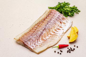 Raw pollock (Pollachius virens) fillet. Fresh fish for healthy food lifestyle. Lemon, parsley, sea salt, chili, black peppercorn