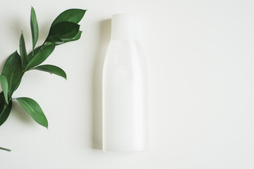 A bottle of micellar water on a white background with a branch of green fresh leaves. The concept...