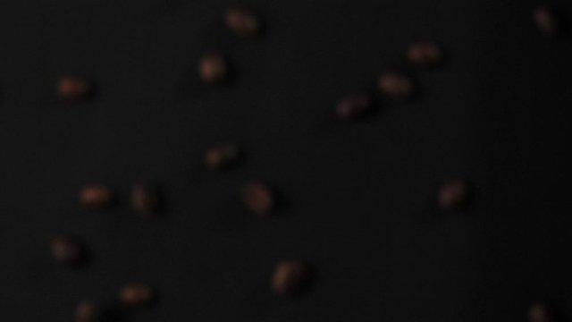 Roasted coffee beans fly after being exploded on black background. Fragrant fresh flying coffee beans. Slow Motion.