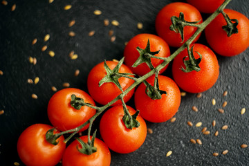 cherry tomatoes on a branch top view on a stone black plate with flax seeds