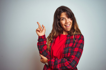 Young beautiful woman wearing red t-shirt and jacket standing over white isolated background with a big smile on face, pointing with hand and finger to the side looking at the camera.