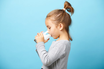 Fototapeta premium Child girl drinks milk without lactose, sideways portrait against blue isolated.