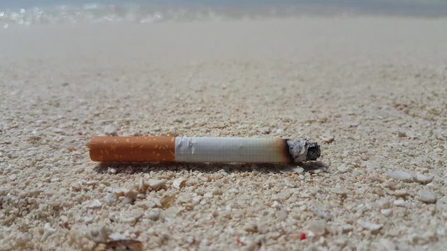 Close up of cigarette burning on white sand beach with blur grey waves background