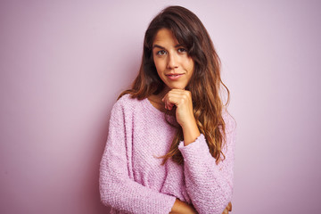 Young beautiful woman wearing sweater standing over pink isolated background looking confident at the camera smiling with crossed arms and hand raised on chin. Thinking positive.