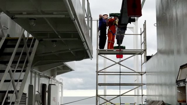 tanker Onyx motorman wearing protective clothes syringes lubricating oil into hoist gear standing on metal ladder ground