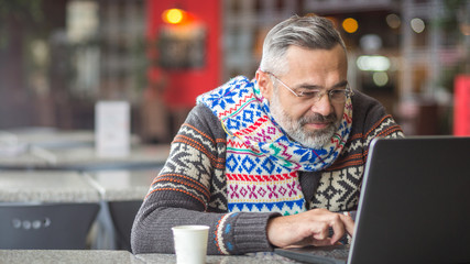  Man wearing autumn or winter clothes, scarf sitting in a cafe working  using laptop