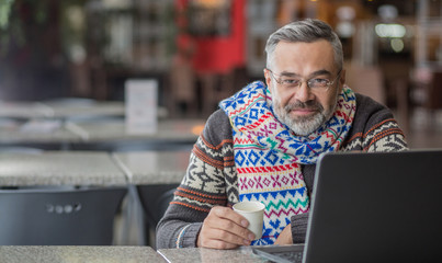  Man wearing autumn or winter clothes, scarf sitting in a cafe working  using laptop
