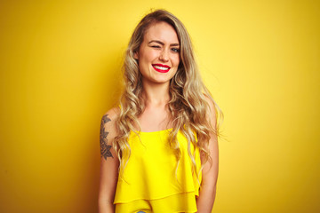 Young attactive woman wearing t-shirt standing over yellow isolated background winking looking at the camera with sexy expression, cheerful and happy face.