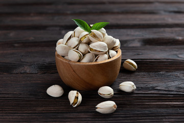  Pistachio in wooden bowl in background with green leaves.