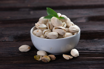  Pistachio in wooden bowl in background with green leaves.