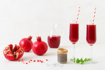 Pomegranates and chia seeds with fresh mint. A glass pitcher of fresh red juice with two full tumblers. An inviting fresh drink on a clean white table background.