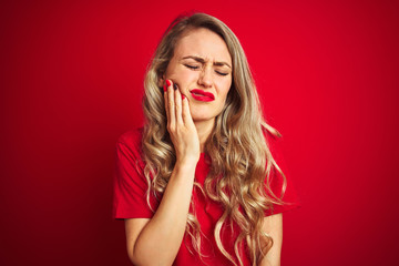 Young beautiful woman wearing basic t-shirt standing over red isolated background touching mouth with hand with painful expression because of toothache or dental illness on teeth. Dentist concept.