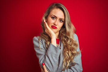 Young beautiful business woman wearing elegant jacket standing over red isolated background thinking looking tired and bored with depression problems with crossed arms.