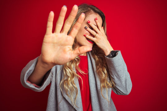 Young beautiful business woman wearing elegant jacket standing over red isolated background covering eyes with hands and doing stop gesture with sad and fear expression. Embarrassed and negative