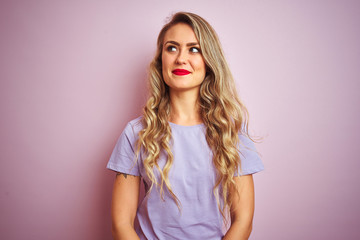 Young beautiful woman wearing purple t-shirt standing over pink isolated background smiling looking to the side and staring away thinking.