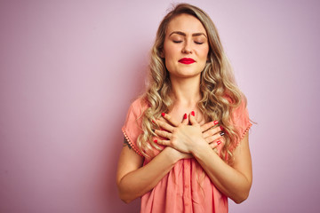 Young beautiful woman wearing t-shirt standing over pink isolated background smiling with hands on chest with closed eyes and grateful gesture on face. Health concept.