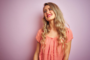 Young beautiful woman wearing t-shirt standing over pink isolated background looking away to side with smile on face, natural expression. Laughing confident.