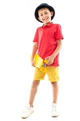 A little boy in panama, yellow jersey, red shorts and white sneakers stands and holds a yellow penny in his hands