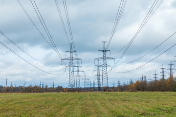 The towers of electric main in the countryside field on the background of blue sky and the forest with the wires