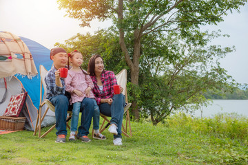 Obraz premium Group of asian family travel and camping at lakeside in forest ,sitting all together and smile. Family and outdoor activity concept.