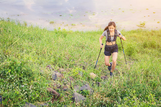 Woman Athlete Runner With Trekking Poles Running Up Mountain Trail Along The River